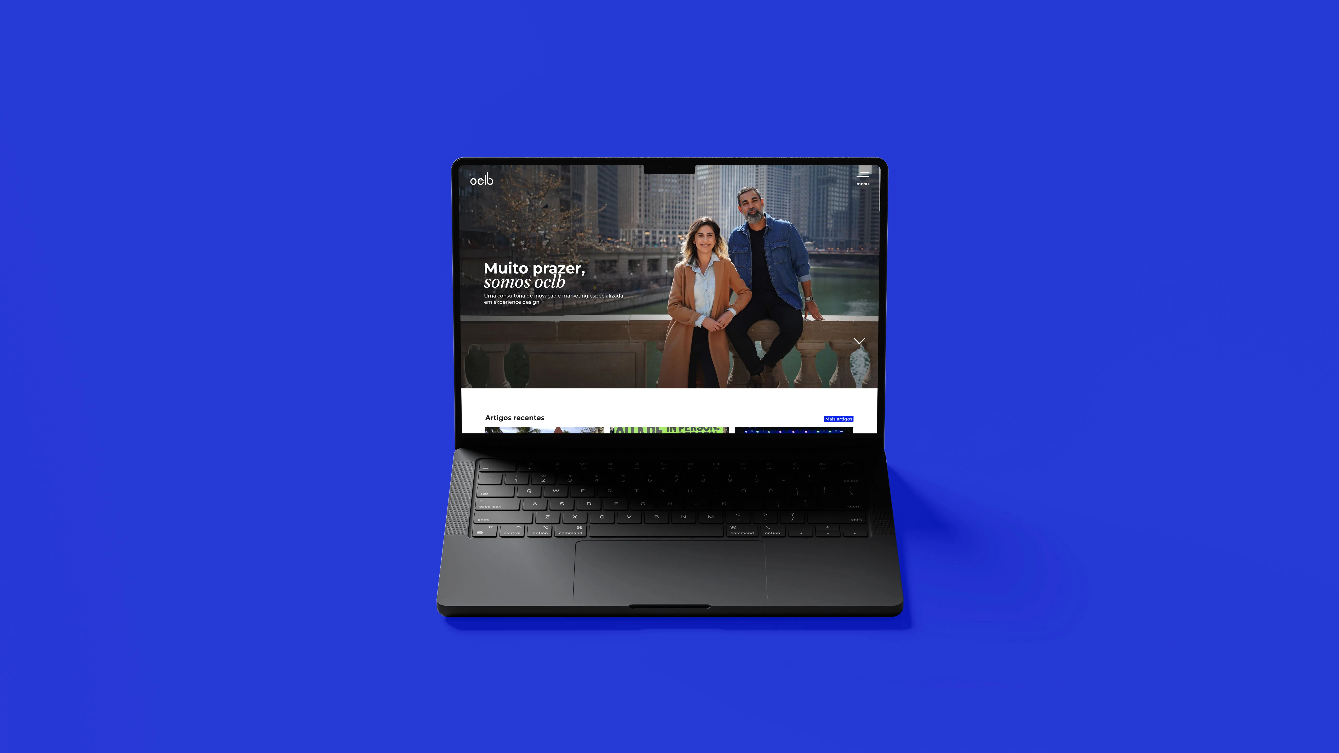 Laptop screen displaying the OCLB homepage with the headline "Muito prazer, somos oclb" over a photo of two people on a bridge, set against a blue background.